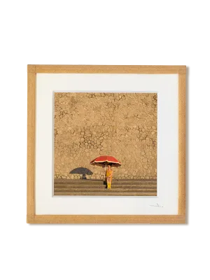tirage photo petit format encadré à la main représentant une femme en bottes jaune assise sous un grand parasol rouge