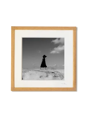 tirage photo petit format encadré à la main représentant une femme en robe noir marchant sur les roches blanches de Milos