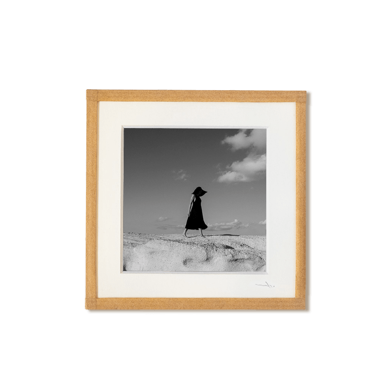 tirage photo petit format encadré à la main représentant une femme en robe noir marchant sur les roches blanches de Milos