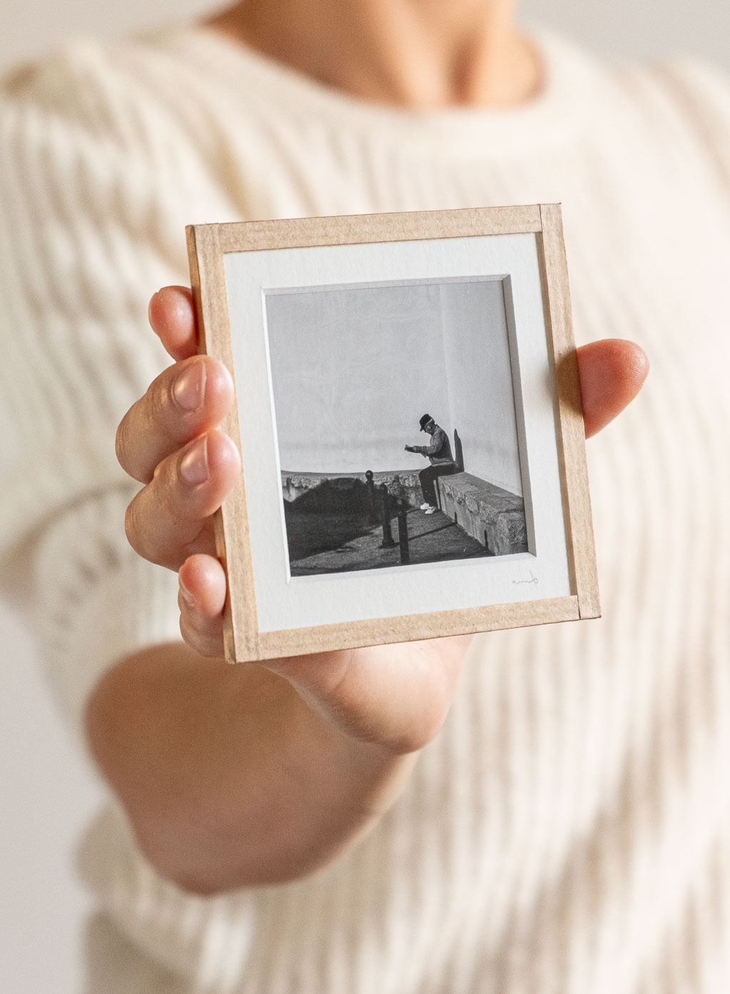 tirage photo petit format encadré à la main représentant un vieil homme assis contre un mur lisant le journal
