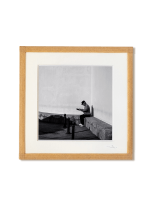 tirage photo petit format encadré à la main représentant un vieil homme assis contre un mur lisant le journal