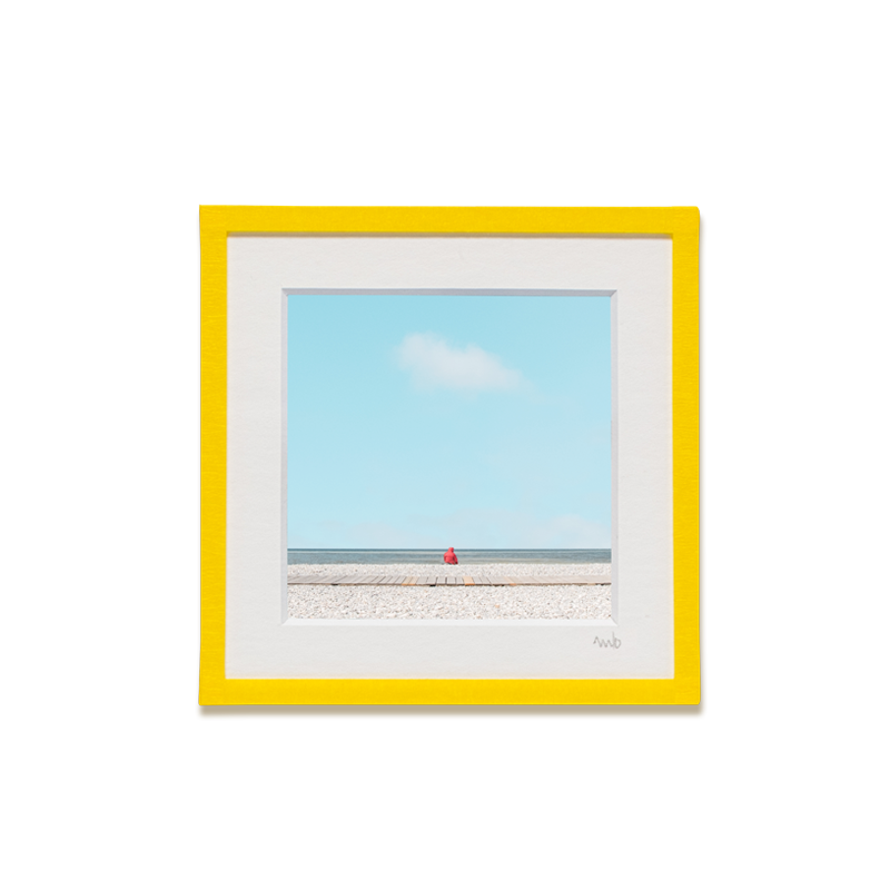 tirage photo petit format encadré à la main représentant un petit personnage rouge assis face à l'océan avec ciel bleu et un nuage