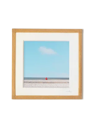tirage photo petit format encadré à la main représentant un petit personnage rouge assis face à l'océan avec ciel bleu et un nuage