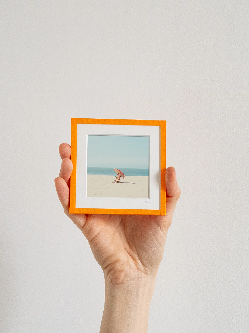 tirage photo petit format encadré à la main représentant un homme assis sous un parasol orange sur la plage d'Ostende