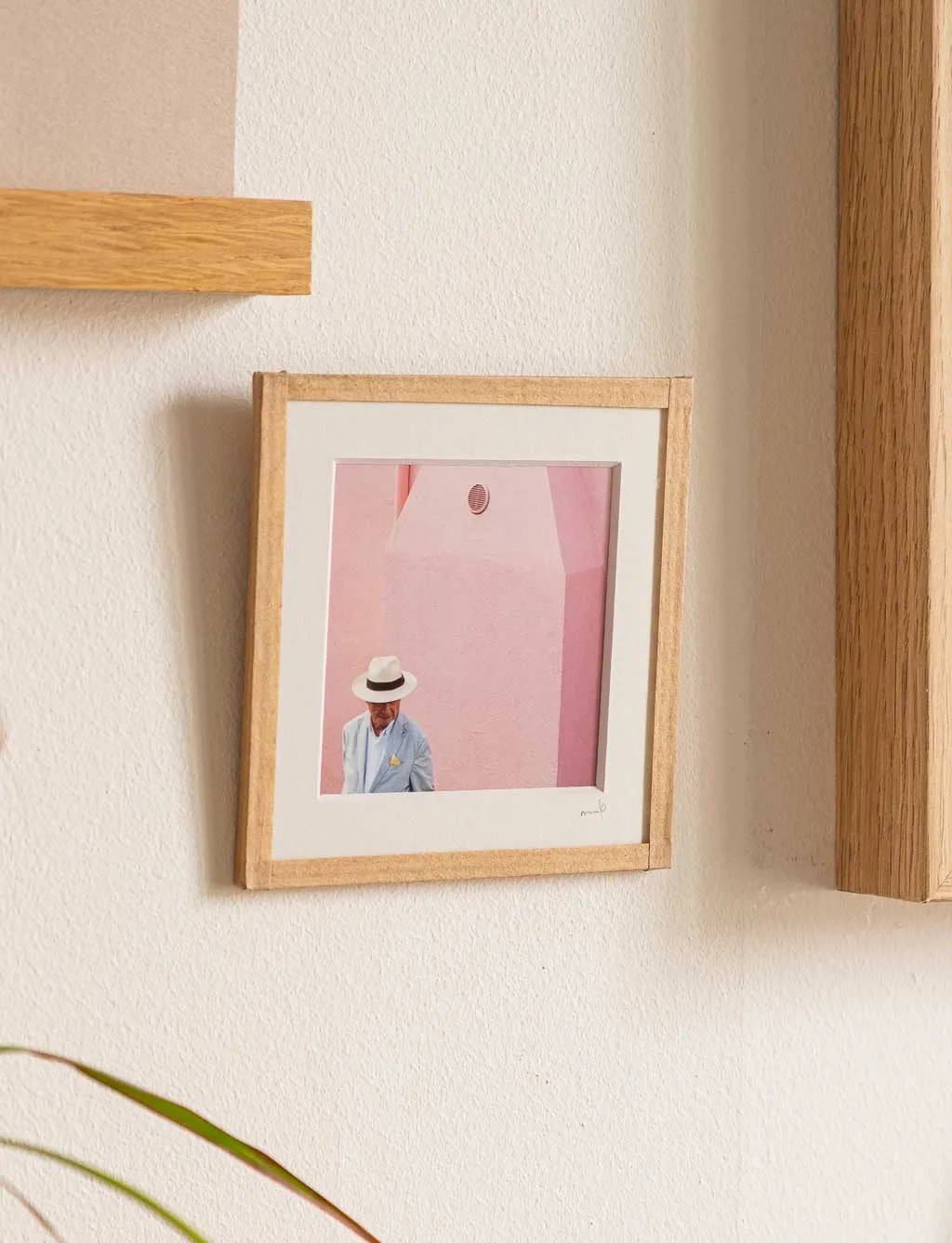 tirage photo petit format encadré à la main représentant un homme portant une chapeau Panama devant un mur rose