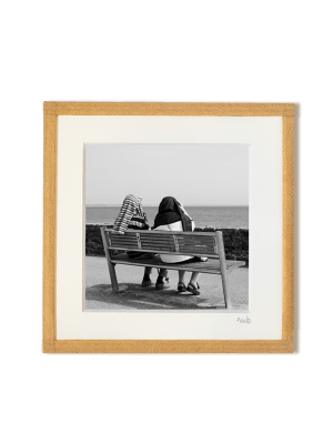 tirage photo petit format encadré à la main représentant un couple de dos assis sur un banc face à la mer, des pulls sur la tête