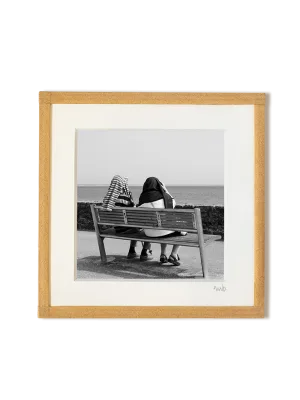 tirage photo petit format encadré à la main représentant un couple de dos assis sur un banc face à la mer, des pulls sur la tête