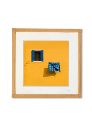 tirage photo petit format encadré à la main représentant une façade jaune avec une fenetre et un torchon bleu qui seche