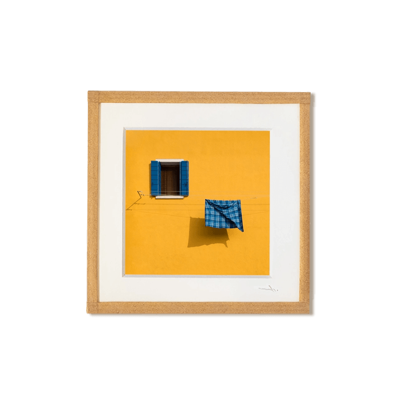 tirage photo petit format encadré à la main représentant une façade jaune avec une fenetre et un torchon bleu qui seche