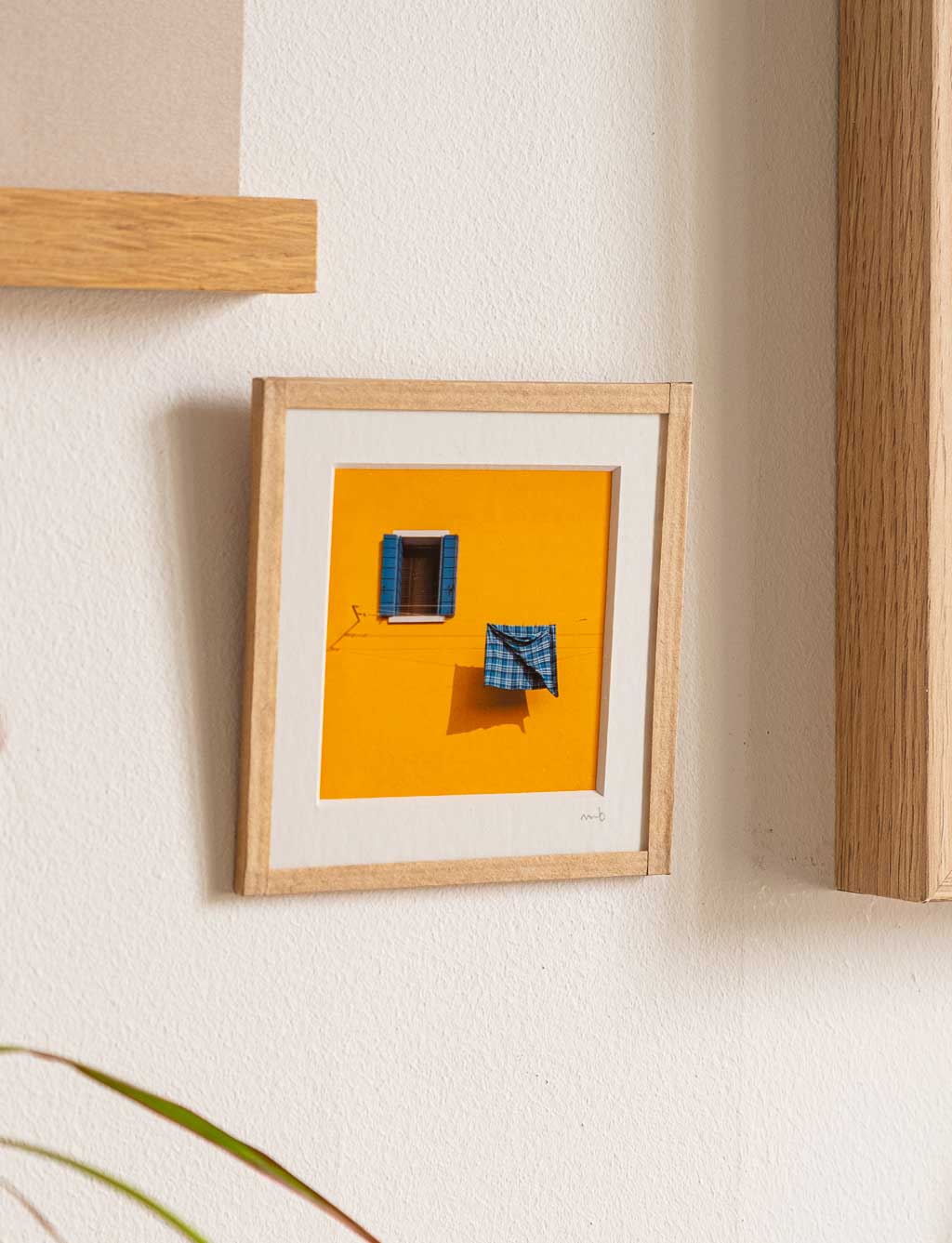 tirage photo petit format encadré à la main représentant une façade jaune avec une fenetre et un torchon bleu qui seche