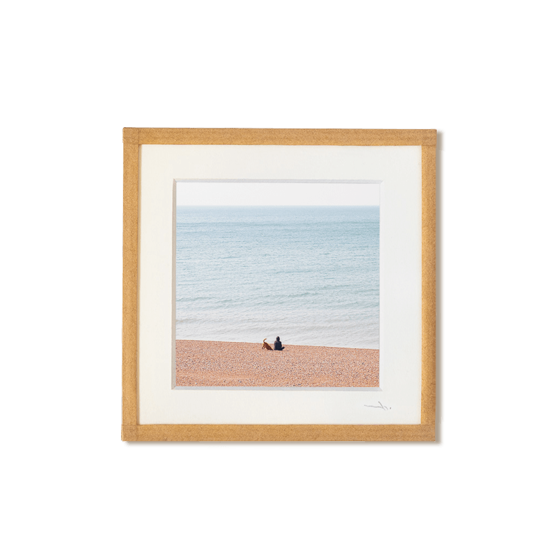 tirage photo petit format encadré à la main représentant un homme et son chien assis sur une plage de galets à Brighton