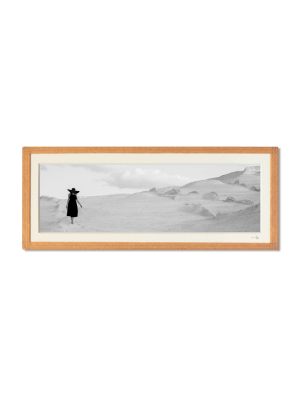 tirage photo petit format encadré à la main représentant une femme en robe et chapeau noir marchant sur les rochers blancs de Milos