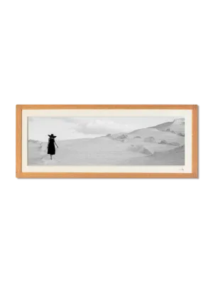 tirage photo petit format encadré à la main représentant une femme en robe et chapeau noir marchant sur les rochers blancs de Milos
