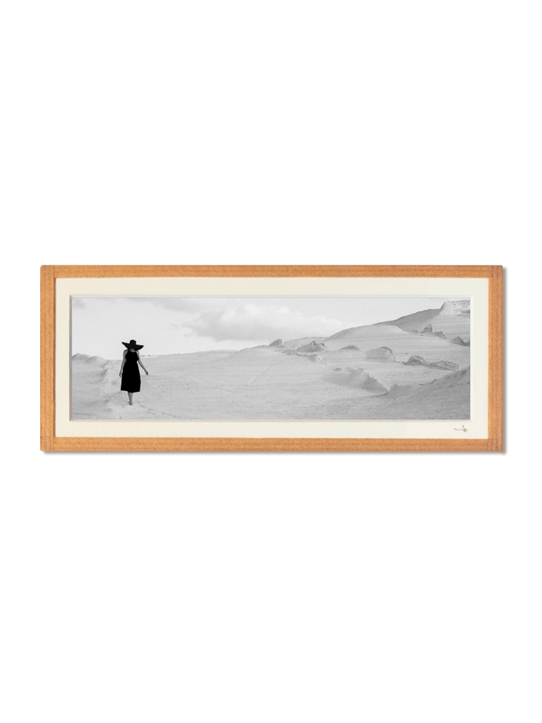 tirage photo petit format encadré à la main représentant une femme en robe et chapeau noir marchant sur les rochers blancs de Milos